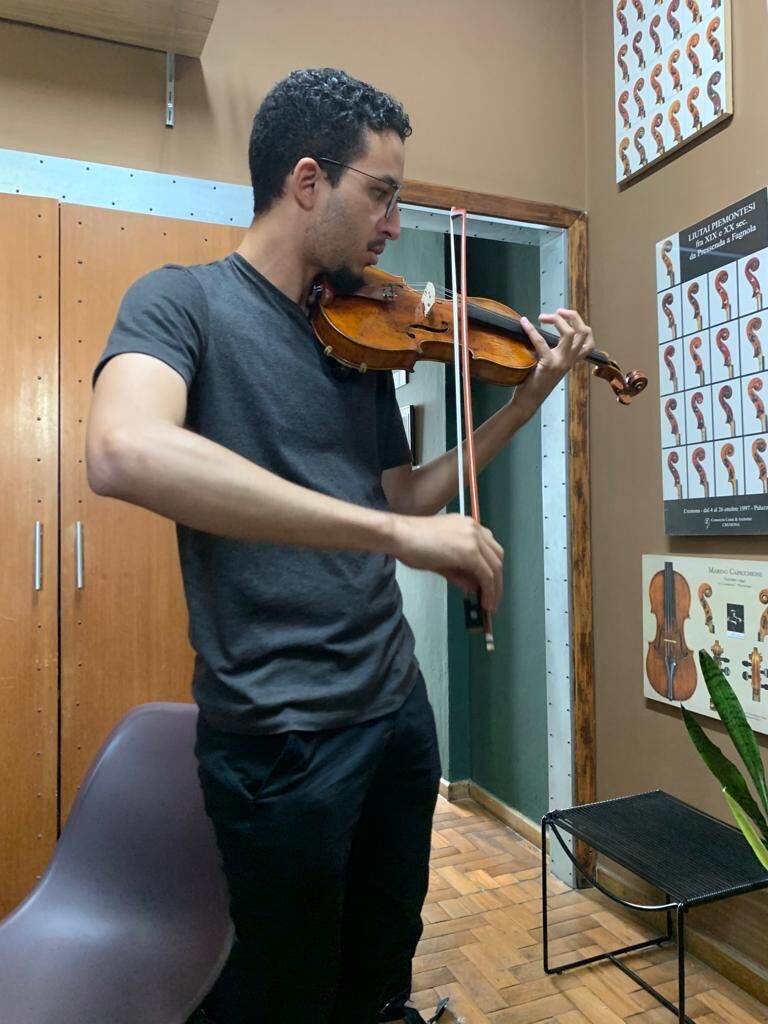 André tocando viola em pé num ateliê de luthieria