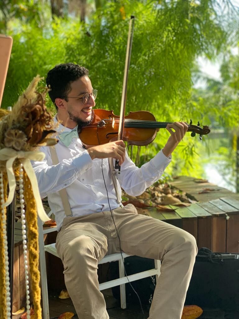 André tocando viola sorrindo, numa cerimônia ao ar livre