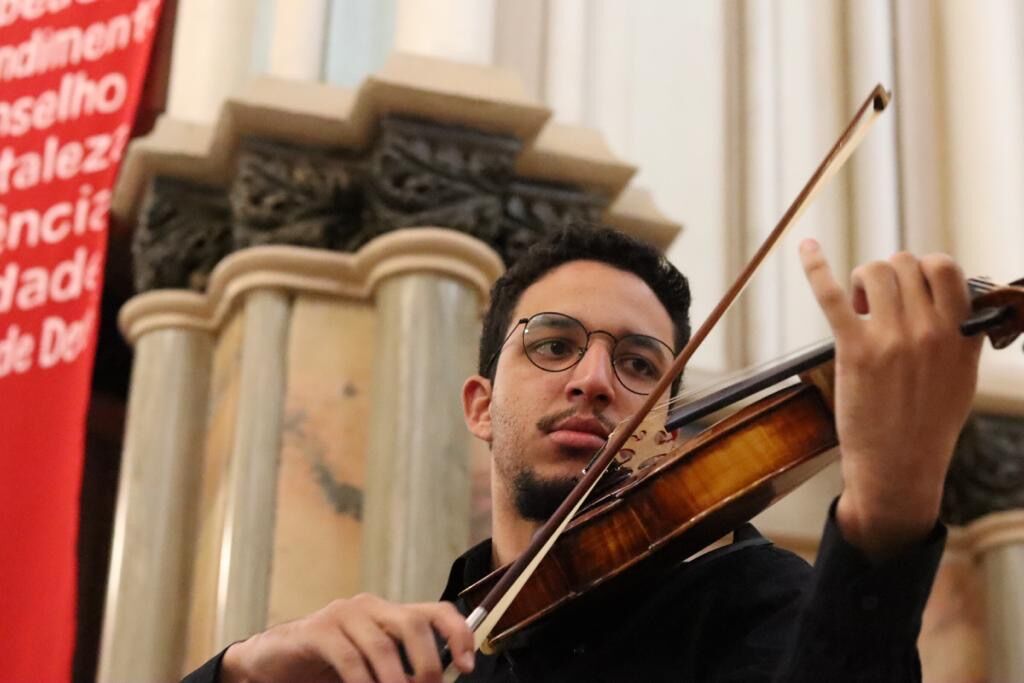 André tocando viola em concerto, diante de colunas de pedra