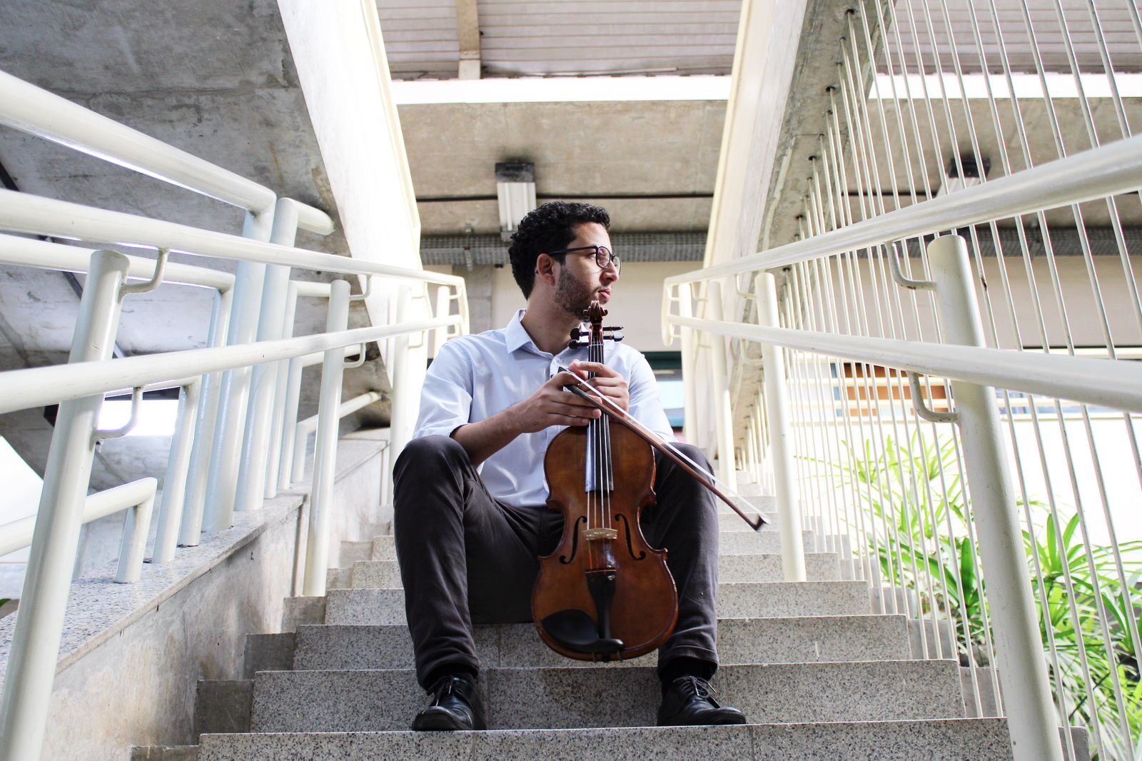 André Vieira sentado numa escada, segurando a viola e o arco