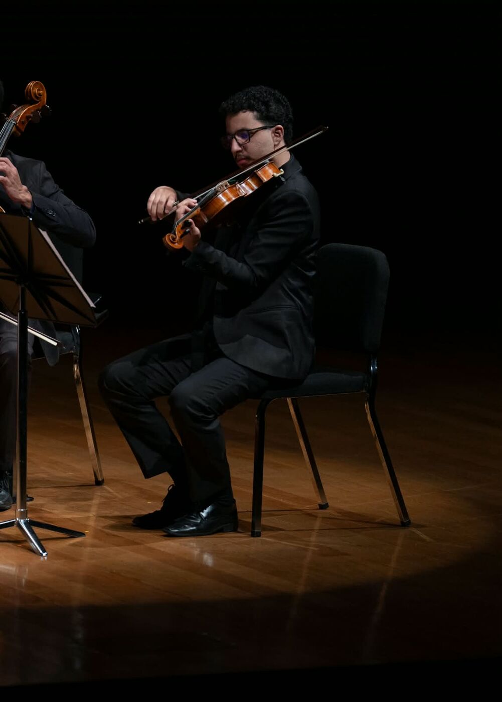 André tocando viola sentado, sob um foco de luz no palco