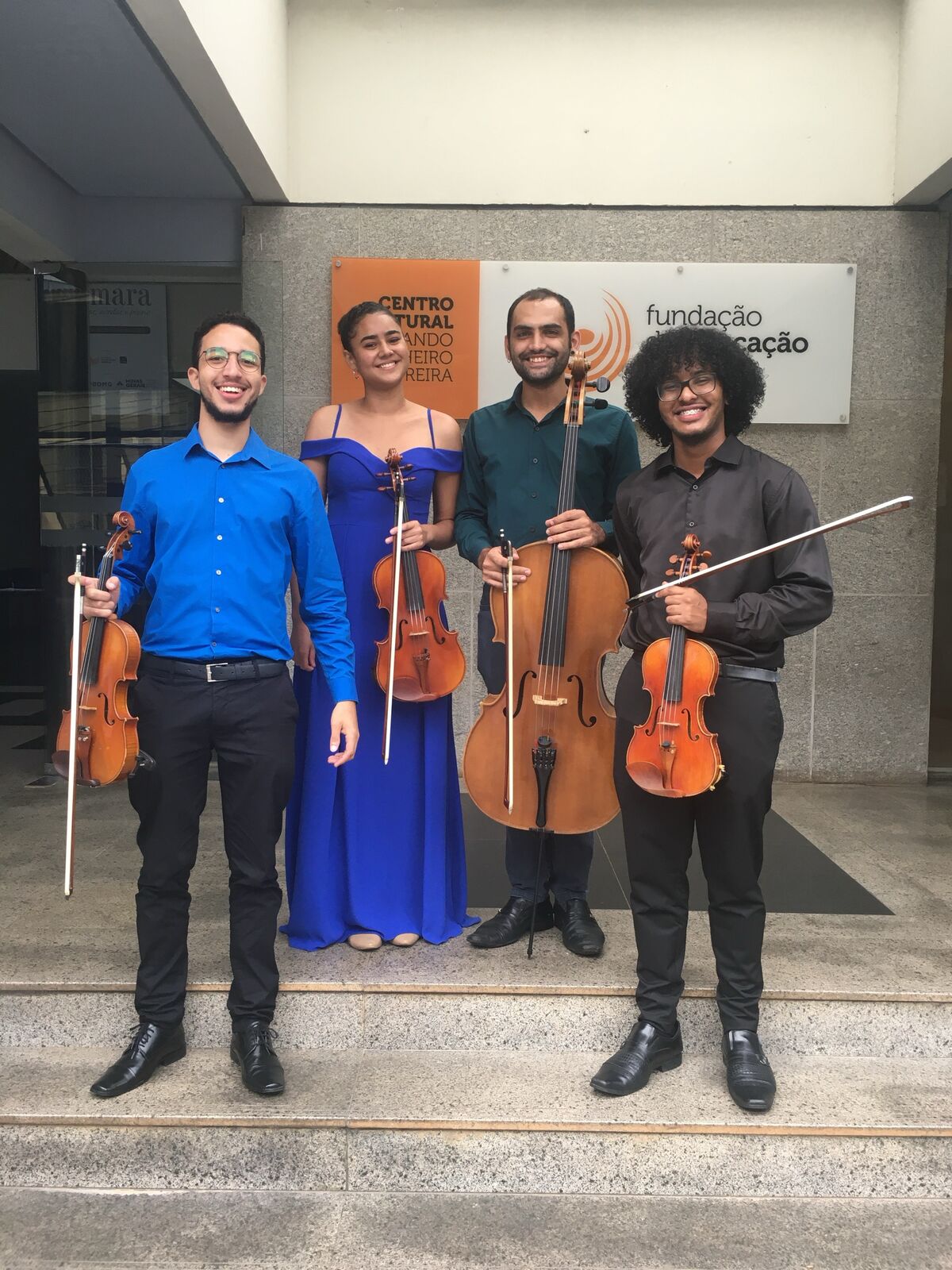 Quarteto de cordas posando com os instrumentos na entrada de um centro cultural